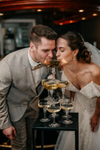 Brautpaar trinkt gemeinsam aus einem Champagner Tower - Weddings by Cara.