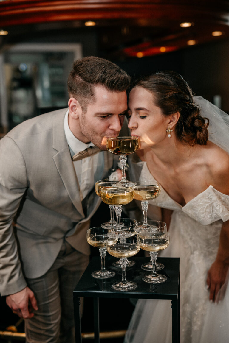 Brautpaar trinkt gemeinsam aus einem Champagner Tower - Weddings by Cara.