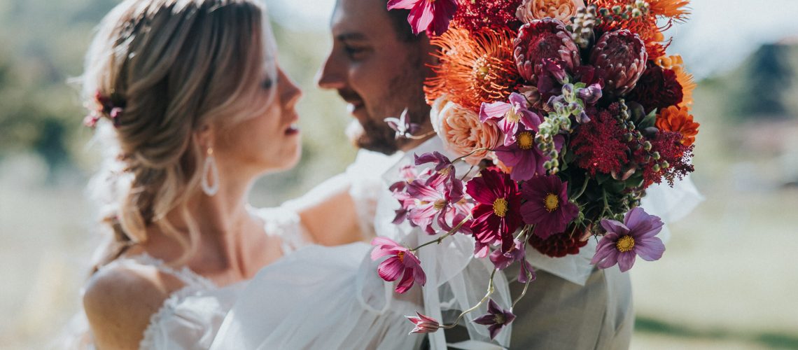 Brautpaar beim Fotoshooting mit einem herbstlichen Brautstrauß im Vordergrund bei ihrer Autumn Sunset Wedding